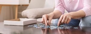 Elderly female hands trying to connect pieces of jigsaw puzzle
